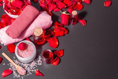 Taze gül yapraklı doğal spa konsepti. Gül tuzu, temel yağ, yumuşak havlular. Modern sert ışık, karanlık gölge. Siyah taş arkaplan, üst görünüm