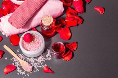 Taze gül yapraklı doğal spa konsepti. Gül tuzu, temel yağ, yumuşak havlular. Modern sert ışık, karanlık gölge. Siyah taş arkaplan, üst görünüm