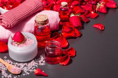 Taze gül yapraklı doğal spa konsepti. Gül tuzu, temel yağ, yumuşak havlular. Modern sert ışık, karanlık gölge. Siyah taş arkaplan, boşluğu kopyala