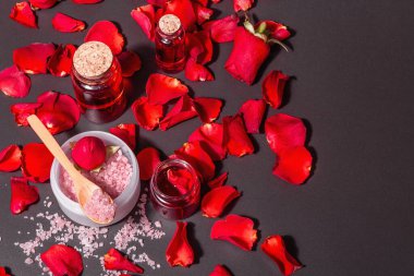Taze gül yapraklı doğal spa konsepti. Gül tuzu, temel yağ, yumuşak havlular. Modern sert ışık, karanlık gölge. Siyah taş arkaplan, üst görünüm