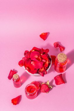 Pembe arka planda gerekli yağ ve gül yaprakları şişeleri. Modaya uygun sert ışık, koyu gölge, üst manzara