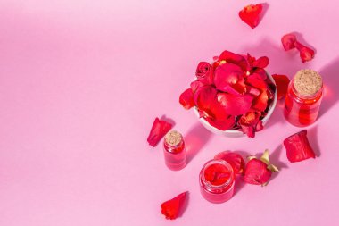 Pembe arka planda gerekli yağ ve gül yaprakları şişeleri. Modaya uygun sert ışık, koyu gölge, üst manzara
