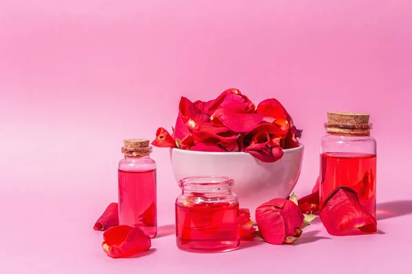 Pembe arka planda gerekli yağ ve gül yaprakları şişeleri. Modaya uygun sert ışık, koyu gölge, metin için yer