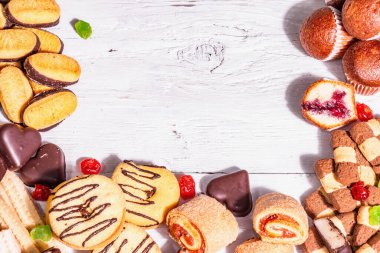 Çeşitli kurabiyeler ve kekler. Modaya uygun sert ışık, karanlık gölge. Beyaz tahta tahta arka plan, üst görünüm