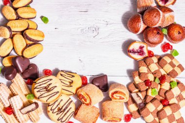 Çeşitli kurabiyeler ve kekler. Modaya uygun sert ışık, karanlık gölge. Beyaz tahta tahta arka plan, üst görünüm