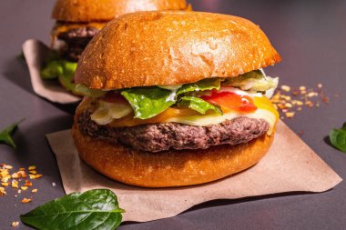 Taze hamburger, Amerikan fast food. İki parçadan oluşuyor, modern sert ışık, karanlık gölge. Dağıtılmış baharatlar, siyah taş beton arka plan, metin için yer