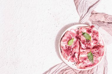 Çiğ domuz eti, dilimlenmiş et. Taze et, kuru sumak, sarımsak ve fesleğen yaprağı. Sağlıklı yemek pişirme konsepti, modaya uygun sert ışık, karanlık gölge. Beyaz macun arkaplan, üst görünüm