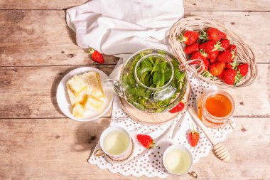 Çay zamanı konsepti. Aromatik nane çayı, olgun çilek, tatlı bal. Sıcak bir içecek, tribünde seramik bardaklar, kaliteli keten peçeteler. Eski tahta arka plan, üst görünüm