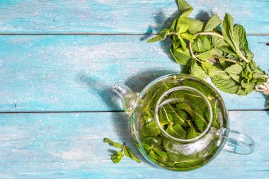 Taze yapraklardan nane çayı. Cam çaydanlıkta sağlıklı sıcak bir içecek. Modern sert ışık, karanlık gölge, turkuaz tahta kaplama arka plan, üst görünüm