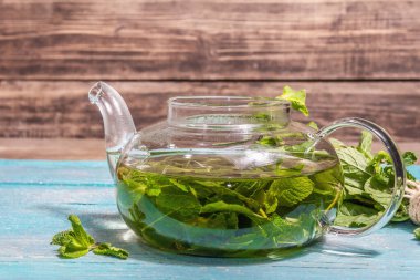 Taze yapraklardan nane çayı. Cam çaydanlıkta sağlıklı sıcak bir içecek. Modern sert ışık, karanlık gölge, turkuaz tahta tahta arka plan, metin için yer