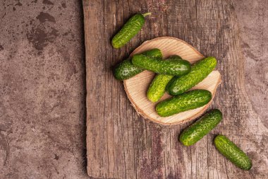 Tahta tezgahta gevrek salatalıklar. Taze yeşil sebzeler, organik çiftçi ürünü. Tahta doğrama tahtası, mermer taş arka plan, üst manzara.