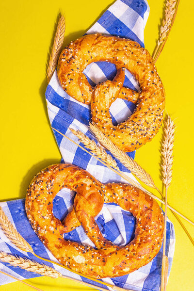 Oktoberfest concept - pretzels on a traditional napkin. Trendy hard light, dark shadow. Dry spikelets, pastel yellow background, place for text