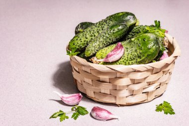 Sepetteki son moda çirkin organik salatalıklar. Taze sebzeler, sarımsak karanfilleri, maydanoz yeşillikleri. Çirkin yemek pişirme konsepti, modern sert ışık, karanlık gölge. Taş beton arkaplan, kopyalama alanı