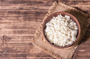 Seramik kasede süzme peynir. Derin bir tabakta ev yapımı süt ürünü. Eski ahşap masa, üst manzara.