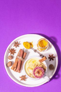 Buzlu altın zerdeçal sütü. Tarçın, hindistan cevizi, anason baharatları. Sağlıklı kahvaltı içeceği konsepti. Modern sert ışık, koyu gölge, pastel eflatun arka plan, üst manzara.