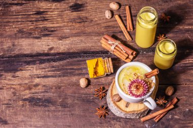 Buzlu altın zerdeçal sütü. Tarçın, hindistan cevizi, anason baharatları. Sağlıklı kahvaltı içeceği konsepti. Modern sert bir ışık, karanlık bir gölge, eski ahşap masa, üst manzara.