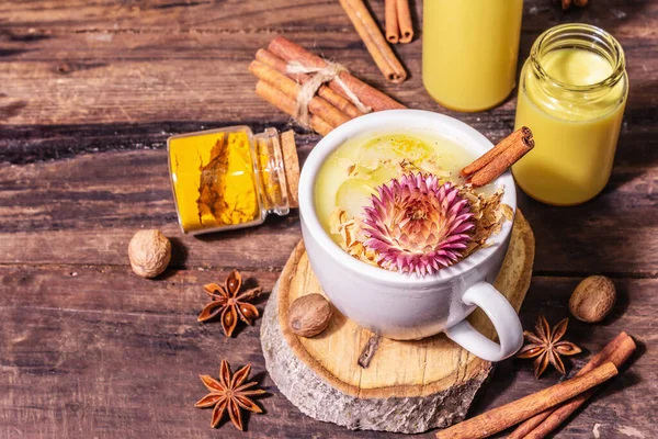 Golden turmeric milk with ice. Cinnamon, nutmeg, anise spices. Healthy morning breakfast drink concept. A modern hard light, dark shadow, old wooden table, copy space