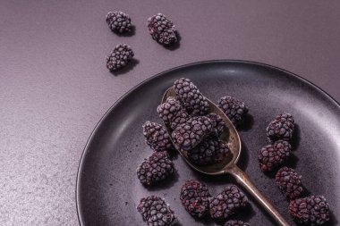 Seramik tabakta böğürtlen. Sağlıklı beslenme için dondurulmuş meyve. Minimalist konsept, siyah taş beton zemin, sert ışık, koyu gölge, düz uzanma