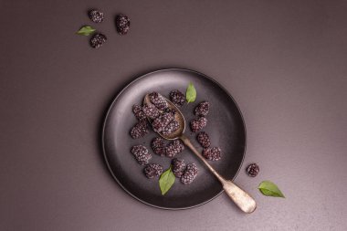 Seramik tabakta böğürtlen. Sağlıklı beslenme için dondurulmuş meyve. Minimalist kavram, siyah taş arkaplan, üst görünüm