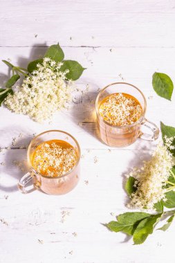 Mürver çiçeği çayı. Taze yaz içkisi, sağlıklı yaşam tarzı konsepti. Modaya uygun sert ışık, karanlık gölge. Eski beyaz tahta arka plan, üst görünüm