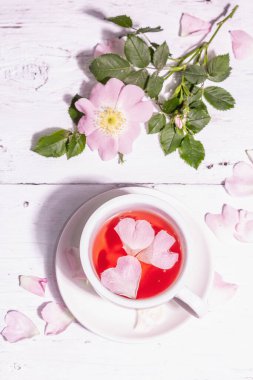 Gül kalça çiçekleri çayı. Yaz vitamini içeceği, sert ışık, karanlık gölge. Beyaz ahşap arkaplan, üst görünüm