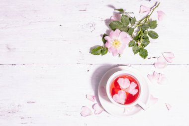 Gül kalça çiçekleri çayı. Yaz vitamini içeceği, sert ışık, karanlık gölge. Beyaz ahşap arkaplan, üst görünüm