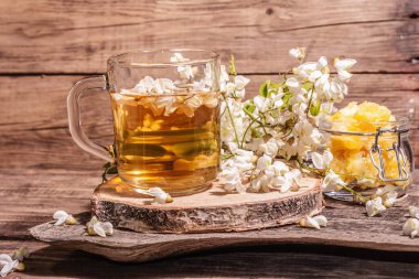 Akasya çiçeklerinden çay. Sağlıklı yaz vitamin içeceği, sert ışık, karanlık gölge. Tatlı balım, eski ahşap ayaklar, yakın çekim