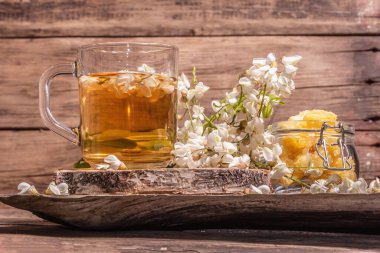 Akasya çiçeklerinden çay. Sağlıklı yaz vitamin içeceği, sert ışık, karanlık gölge. Tatlı balım, eski ahşap ayaklar, yakın çekim