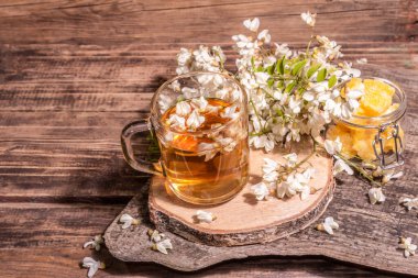 Akasya çiçeklerinden çay. Sağlıklı yaz vitamin içeceği, sert ışık, karanlık gölge. Tatlı bal, eski ahşap stantlar, kopyalama alanı