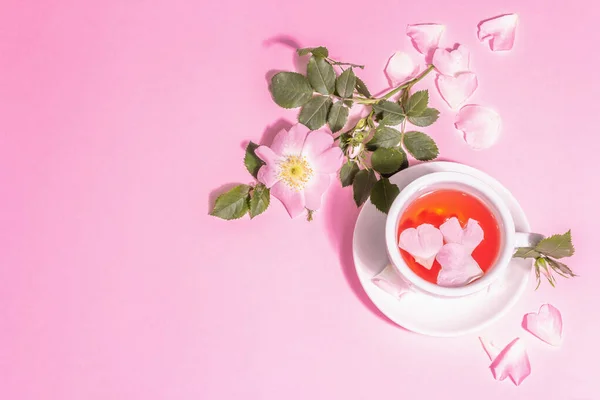 バラの腰の花からお茶 夏のビタミンドリンク ハードライト 暗い影 ピンクのパステルの背景 トップビュー — ストック写真