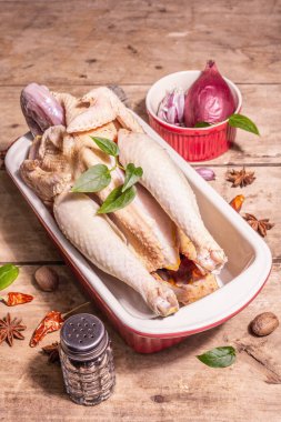 Sağlıklı bir yaşam tarzı için çiğ tavuk leşi. Geleneksel Çin baharatlarıyla seramik pişirme tavasında serbest tarım kuşu. Modaya uygun bir sert ışık, karanlık gölge, eski ahşap masa, boşluğu kopyala