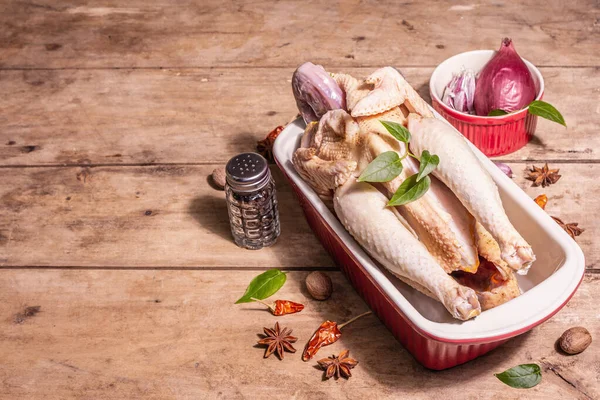 Raw whole chicken carcass for healthy food lifestyle. Free-range farm bird with traditional Chinese spices in ceramic baking pan. A trendy hard light, dark shadow, vintage wooden table, copy space