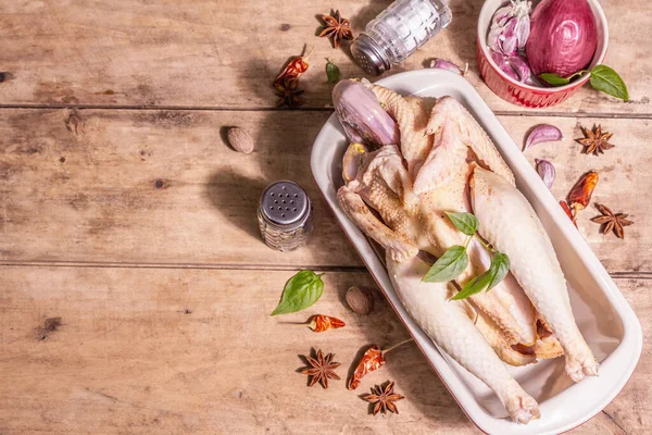 Raw whole chicken carcass for healthy food lifestyle. Free-range farm bird with traditional Chinese spices in ceramic baking pan. A trendy hard light, dark shadow, vintage wooden table, top view
