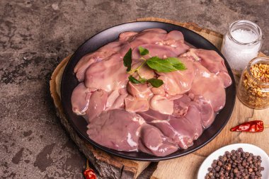 Raw chicken liver. A useful ingredient for preparing healthy food. Spice set, wooden stand. Trendy concrete stone background, close up