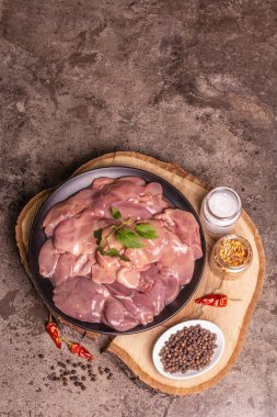 Raw chicken liver. A useful ingredient for preparing healthy food. Spice set, wooden stand. Trendy concrete stone background, top view