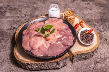Raw chicken liver. A useful ingredient for preparing healthy food. Spice set, wooden stand. Trendy concrete stone background, close up