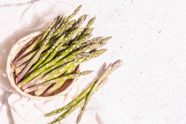 Ripe asparagus in a wicker basket. Fresh green ingredients ready for cooking healthy food. Modern hard light, dark shadow. White plaster background, top view