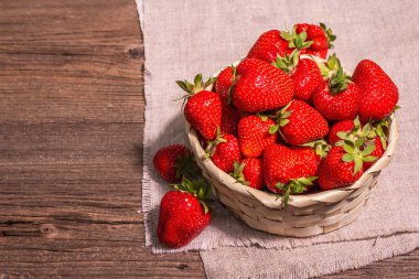 Hasır sepette taze olgun çilek. Tatlı yaz meyveleri, sağlıklı yiyecekler. Modern sert ışık, karanlık gölge. Eski tahta kaplama arka plan