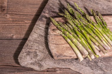 Olgun kuşkonmaz pişirmeye hazır. Klasik ahşap tribünler, sert ışık, karanlık gölge. Eski tahta arkaplan, üst görünüm