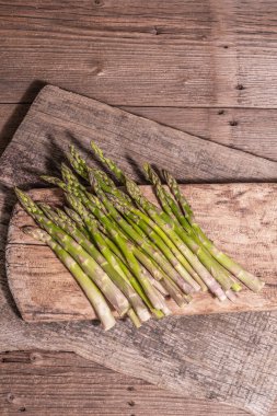 Olgun kuşkonmaz pişirmeye hazır. Klasik ahşap tribünler, sert ışık, karanlık gölge. Eski tahta arkaplan, üst görünüm