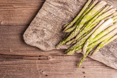Olgun kuşkonmaz pişirmeye hazır. Klasik ahşap tribünler, sert ışık, karanlık gölge. Eski tahta arkaplan, üst görünüm