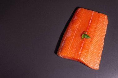 Taze çiğ somon ya da alabalık filetosu. Siyah taş arka planda. Sağlıklı yiyecekler için kullanışlı bir malzeme, Omega 3 kaynağı. Modern sert bir ışık, karanlık bir gölge, mutfak kağıdı, üst görünüm.