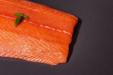 Taze çiğ somon ya da alabalık filetosu. Siyah taş arka planda. Sağlıklı yiyecekler için kullanışlı bir malzeme, Omega 3 kaynağı. Modern sert bir ışık, karanlık bir gölge, mutfak kağıdı, üst görünüm.