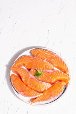 Taze çiğ somon ya da balık fileto bifteği. Minimalist tasarım, modern sert ışık, karanlık gölge. Sağlıklı deniz ürünleri pişirmek için soğutulmuş malzemeler. Beyaz macun mutfak arka planı, üst görünüm