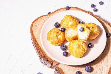 Yabanmersinli profiterol. Kremalı pasta, pasta, ahşap tezgahta kremalı pasta, modaya uygun sert ışık, koyu gölge. Beyaz alçı arkaplan, kopyalama alanı