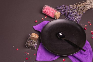 Tatlı bir tatlı için masa hazırlıyorum. Tabak, kaşık, lavanta çiçekleri, gül yaprakları ve tatlı pembe şeker. Siyah taş arkaplan, boşluğu kopyala