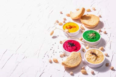 Çeşitli humus sosları, ıspanak, pancar kökü, zerdeçal ve sebzelerle farklı renklerde humus yatağı, vejetaryen atıştırmalıkları. Beyaz macun arkaplanı, kopyalama alanı