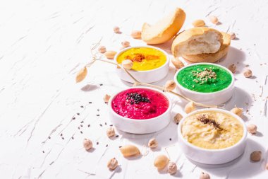 Çeşitli humus sosları, ıspanak, pancar kökü, zerdeçal ve sebzelerle farklı renklerde humus yatağı, vejetaryen atıştırmalıkları. Beyaz macun arkaplanı, kopyalama alanı