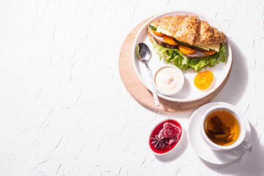 Sağlıklı kahvaltı konsepti. Günaydın, çay, kruvasan ve çilek reçeli. Modaya uygun sert ışık, koyu gölge, beyaz macun arkaplan, üst görünüm