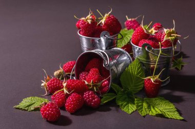 Siyah taştan bir arka planda olgun ahududular. Küçük kovalar, taze yapraklar, yeni hasat. Modaya uygun sert ışık, karanlık gölgeler, metin için yer